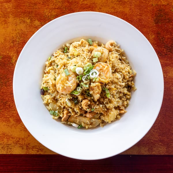 A white bowl filled with shrimp fried rice, garnished with green onions, on a rustic orange table.