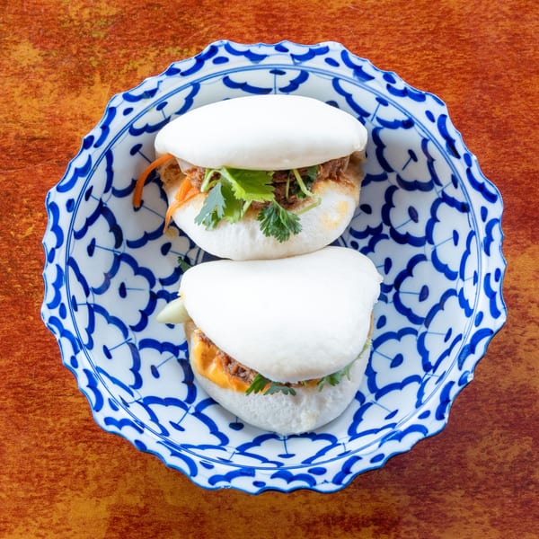 Two bao buns filled with meat, cilantro, and carrots, served on a blue and white patterned plate.