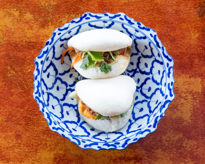 Two bao buns filled with meat, cilantro, and carrots, served on a blue and white patterned plate.