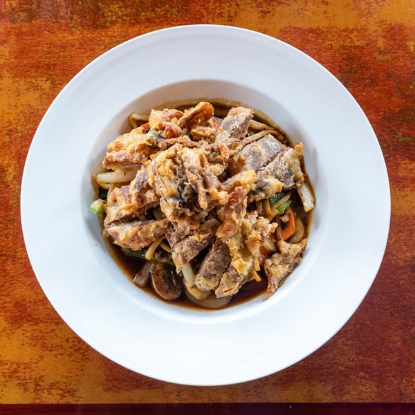 Top-down view of a white bowl filled with crispy fried soft-shell crab over noodles and vegetables.