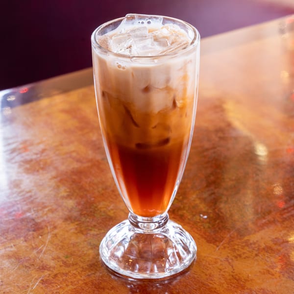 Iced Thai tea with milk and ice in a tall glass on a wooden table.