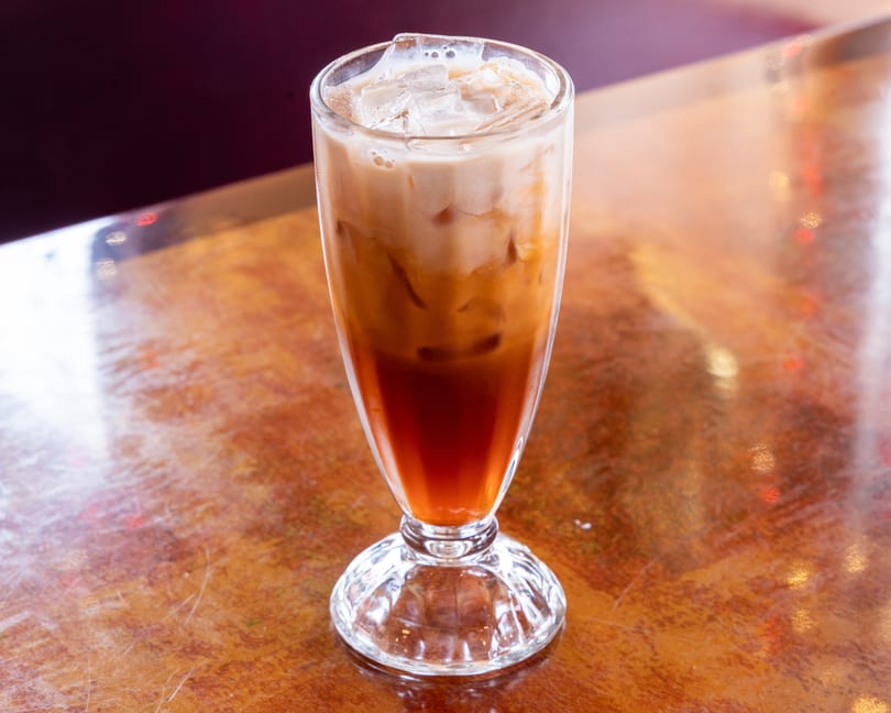 Iced Thai tea with milk and ice in a tall glass on a wooden table.