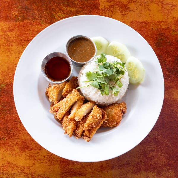 Crispy fried chicken, white rice with cilantro, cucumber slices, and two dipping sauces on a white plate.