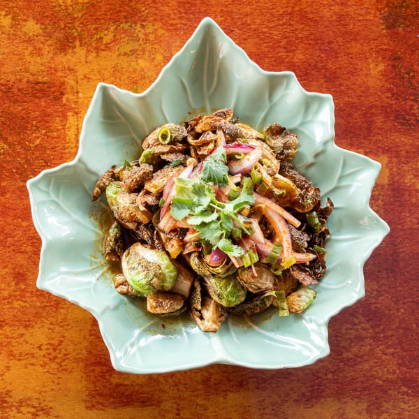 Crispy Brussels sprouts with red onions, green onions, and cilantro in a light blue leaf-shaped bowl.