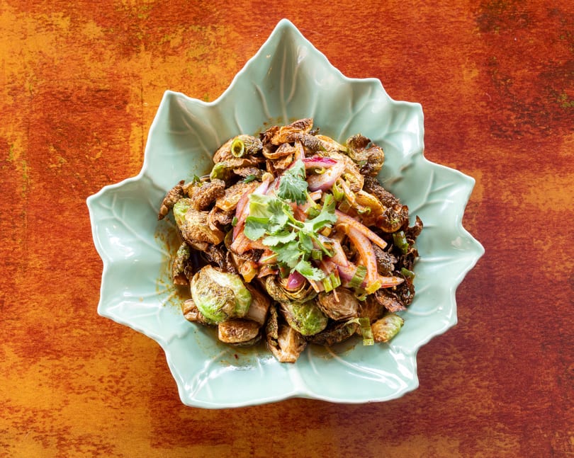 Crispy Brussels sprouts with red onions, green onions, and cilantro in a light blue leaf-shaped bowl.