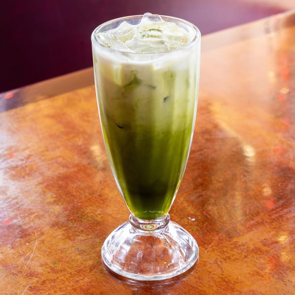 Iced matcha latte with a layer of white milk on top, served in a tall glass on a wooden table.