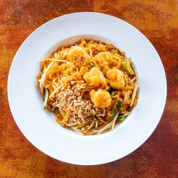 Pad Thai with shrimp, bean sprouts, and crushed peanuts in a white bowl on a rustic table.