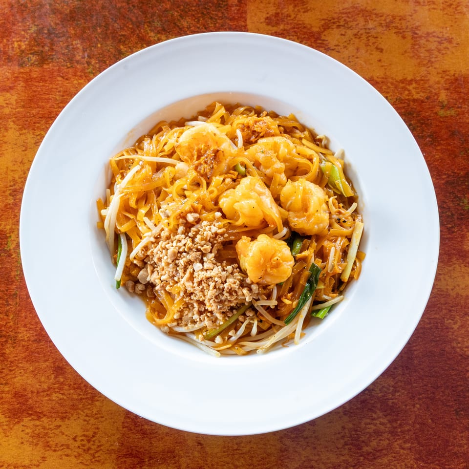 Pad Thai with shrimp, bean sprouts, and crushed peanuts in a white bowl on a rustic table.