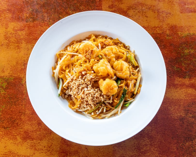 Pad Thai with shrimp, bean sprouts, and crushed peanuts in a white bowl on a rustic table.